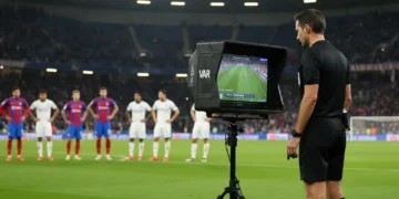 Árbitro de futebol revisando lance no monitor VAR durante uma partida, com foco na tecnologia.