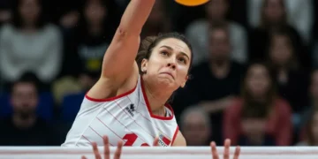 Jogador de vôlei atacando a bola sobre a rede em uma partida intensa.