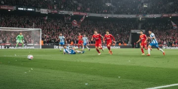 Jogadores de futebol em ação, atacando o gol adversário em um campo iluminado à noite.